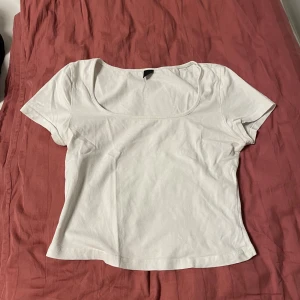 Vit croppad topp med rund hals - En enkel och stilren vit topp med croppad passform och rund, djup urringning. T-shirten har korta ärmar och är tillverkad i mjuk bomull, perfekt för en clean och fräsch look. Passar till allt