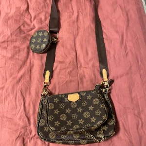 Brun axelväska - Cool brun axelväska med flera fack och avtagbar rund myntplånbok. Väskan har guldiga detaljer, kedja och justerbar axelrem. Oanvänd