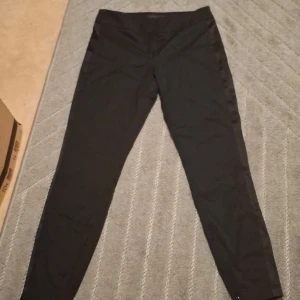 Svarta kostymbyxor från Stockh LM - Svarta kostymbyxor från Stockh LM i klassisk rak modell. Byxorna har dragkedja och knappstängning framtill samt en diskret midja. Perfekta för en clean och stilren look. Materialet känns mjukt och har en lätt stretch.