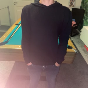 Svart stickad hoodie med huva - En svart stickad hoodie med huva och långa ärmar. Tröjan har en enkel och clean look utan synliga loggor eller detaljer, perfekt för dig som gillar basic och stilrent. Passformen är normal och materialet känns mjukt och bekvämt.