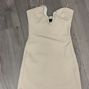 Beige axelbandslös klänning från Zara - 4772/234/250 artikelnummer på zara. Snygg beige axelbandslös kortklänning från Zara med glittrande pärldetaljer längs den v-ringade urringningen. Klänningen har en figurnära passform och tunna axelband, perfekt för dig som vill sticka ut med en elegant look. Aldrig använd!!!!!