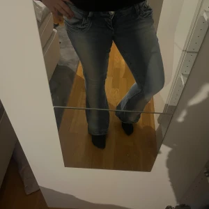 Blå bootcut jeans med slitningar - Snygga blå jeans med bootcut-modell och markerade slitningar framtill. Jeansen har klassisk femficksdesign, knapp och dragkedja i gylfen. Perfekt för dig som gillar en retro vibe och vill ha ett par jeans som sticker ut lite extra.