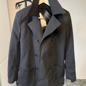 Svart skepparkavaj  - Svart skepparkavaj med bred krage och stora framfickor. 