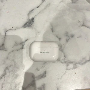 Samsung Galaxy Buds (laddningsetui) - Samsung Galaxy Buds laddningsetui i vitt. Skalet har synliga repor och smuts, men är i övrigt helt. Perfekt som reservdel eller extra etui. Kompatibel med Galaxy Buds-serien. Hörlurar ingår ej.