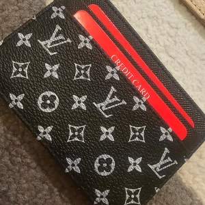  svart korthållare - Snygg svart korthållare från L med klassiskt monogrammönster i vitt. Tillverkad i präglat skinn med plats för flera kort. Perfekt accessoar för dig som vill ha stil och funktion i ett.