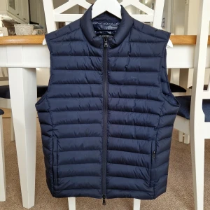 J Lindeberg lättvikts dunväst - Mkt fin marinblå dunväst som knappt är använd.. Stl herr medium. Passar även umgdom. Slim fit, modell "Mick light weight".