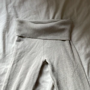 Grå ribbade mjukisbyxor Gina Tricot - Mysiga grå mjukisbyxor från Gina Tricot med bred ribbad midja och raka ben. Byxorna är tillverkade i ett mjukt material som känns skönt mot huden och har en enkel, stilren look. Perfekta för chill dagar hemma eller när du vill vara extra bekväm.