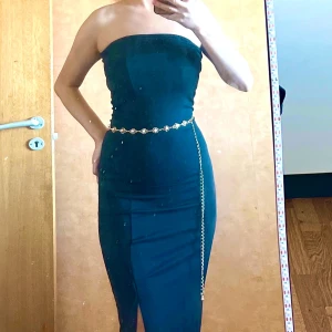 Svart långklänning med slits 2 in 1  med midjakedja  - Snygg svart långklänning med slits på sidan och tight passform. Klänningen är axelbandslös men har även ett alternativ med halterneck. Materialet är mjukt och följsamt, perfekt för dig som vill ha en stilren och elegant look. Passar dig som gillar minimalistisk stil.