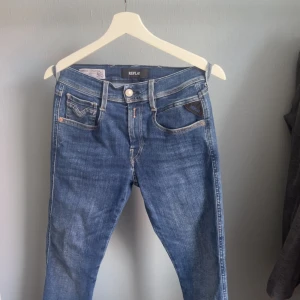 Replay Anbass blå jeans, storlek 27 - Snygga blå jeans från Replay, modell Anbass. Klassisk femficksdesign med ljus tvätt och kontrastsömmar. Jeansen har normal passform och är tillverkade i stretchigt jeansmaterial för extra komfort. Perfekta till sneakers eller boots.