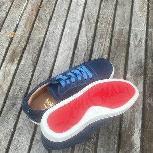 Blåa Christian Louboutin sneakers - Säljer ett par blåa sneakers från Christian Louboutin med klassisk röd sula och blå snörning. Skorna är i mocka och har vita sulor med märkets logga undertill. Snygg och stilren design som sticker ut med den ikoniska röda undersidan.
