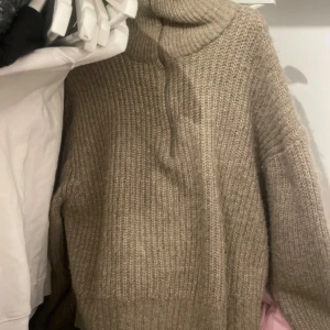 Beige stickad  - Säljer en chunky beige stickad polotröja med half zip-dragkedja. Tröjan har en hög krage och är långärmad, perfekt för kyliga dagar. Den grova stickningen ger en mysig och trendig look.
