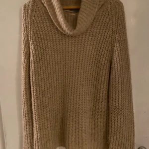 Beige stickad polotröja - Mysig beige stickad polotröja med grovstickad struktur och hög krage. Perfekt för kyliga dagar och enkel att matcha med jeans eller kjol. Långärmad och loose fit för en avslappnad stil. Lite noppig i övrigt fint skick.