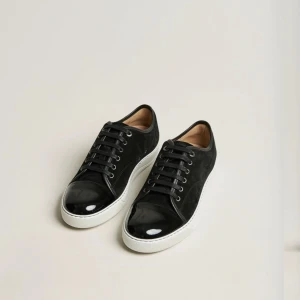 Söker!!!! - Stilrena svarta sneakers med vit sula och snörning. Ovandelen är i mocka och tån är i blankt lackskinn för en snygg kontrast. Perfekta för dig som gillar en clean look med en twist.