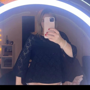 Svart blus i spets med trekvartsärm - Svarts blus blommigt spetsmönster och trekvartsärmar. Blusen har rund halsringning och ärmarna är lite vida. Supersöt!