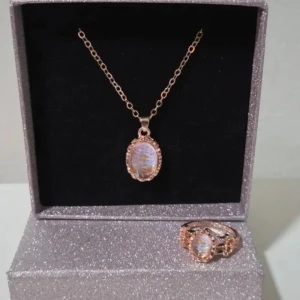 Set med halsband och ring i roséguld - Säljer ett snyggt smyckeset med halsband och matchande ring i roséguld. Båda har en oval, skimrande sten i mitten omgiven av små glittriga detaljer. Kedjan är tunn och elegant, och ringen har samma stendesign. Perfekt för dig som gillar unika accessoarer. Halsbandet är ca 48 cm långt och ringen är 16.5 (Storlek 6)