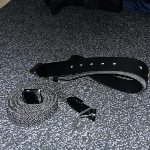 Svart skärp och svart/grå flätat bälte - Två snygga bälten säljes! Ett klassiskt svart bälte i skinn med silverfärgat spänne och ett grått flätat bälte med svarta detaljer och metallspänne. Perfekt för att ge outfiten en clean och stilren touch. Och detta bälte tillbehör grisch bälte