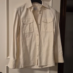 Krämvit overshirt från & Other Stories - Krämvit overshirt från & Other Stories med två stora bröstfickor och knappar framtill. Skjortan är tillverkad i ett strukturerat bomullstyg med siden och linne och har klassisk krage samt långa ärmar med manschett. Perfekt för lager-på-lager och stilren look.