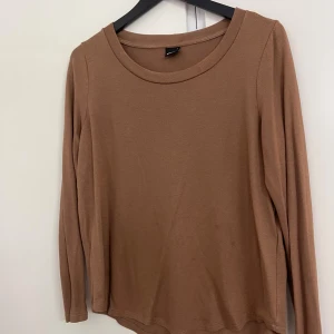 Brun långärmad tröja Gina Tricot - En basic brun långärmad tröja från Gina Tricot i storlek L. Tröjan har rund halsringning och är tillverkad i mjukt bomullsmaterial. Perfekt att styla med jeans eller kjol för en enkel och snygg look.
