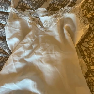 Vit spetsklänning från Amisu - Säljer en vit kort klänning från Amisu med tunna axelband och vacker spetsdetalj längs urringningen. Klänningen har en mjuk, slät yta och känns riktigt fräsch och somrig. Perfekt för dig som gillar en enkel men ändå romantisk stil.