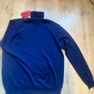 Mörkblå polotröja från Hugo Boss XL - Snygg mörkblå polotröja från Hugo Boss i storlek XL. Tröjan har klassisk polokrage och är långärmad, perfekt för lager-på-lager. Tillverkad i mjuk bomull som känns skön mot huden. Enkel och stilren design som funkar till många outfits. Aldirg använd.