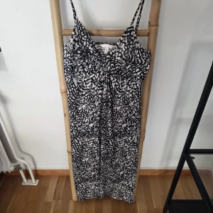 Svartvit långklänning från H&M - Snygg långklänning från H&M med svartvitt abstrakt mönster. Klänningen har smala axelband och en lätt v-ringad överdel. Tillverkad i mjukt och luftigt material, perfekt för varma dagar. Sitter skönt och har en avslappnad passform.