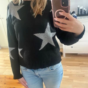Svart stickad tröja med stjärnor - Svart stickad tröja med stora grå stjärnor över hela tröjan. Rund halsringning och långa ärmar med ribbade muddar. Perfekt för dig som gillar en cool och avslappnad stil.