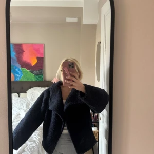 Marinblå kort kappa med stor krage - Mysig mörkblå teddyjacka från Ginatricot med oversized passform och stor, bred krage. Jackan är tillverkad i ett fluffigt teddy-material och har långa ärmar. Perfekt för att hålla värmen under kyliga dagar.