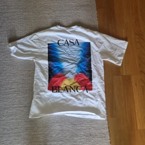 CasaBlanca t-shirt - Vit t-shirt från Casa Blanca med färgstarkt grafiskt tryck i blått, rött och gult på både bröstet och ryggen. Klassisk passform med rund hals och korta ärmar. Perfekt statement-plagg för dig som gillar streetwear och snygga prints.