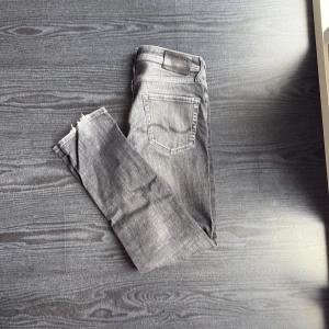 Grå jeans från Jack & Jones - Snygga grå jeans från Jack & Jones med slitna detaljer vid bensluten. Det är modell Tapered/Mike och i storlek /31/32 