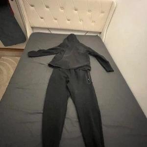 Svart Nike hoodie med dragkedja M - Svart hoodie från Nike i storlek M med dragkedja framtill och huva. Tröjan har långa ärmar och snörning i midjan. Perfekt för chill eller träning, klassisk och enkel design med Nike-logga på benet.