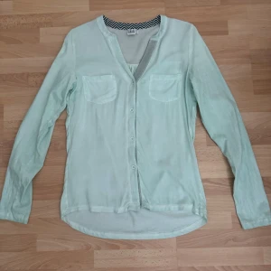 Ljusgrön henley från Saint Tropez - Ljusgrön henley-skjorta från Saint Tropez med v-ringning, knappar framtill och två bröstfickor. Skjortan har lång ärm och är tillverkad i ett mjukt, tunt viskostygg. Perfekt för dig som gillar en clean och chill stil. Använd en gång.