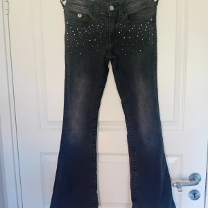 Svarta bootcut jeans med pärlor H&M - Snygga svarta jeans från H&M med utsvängda ben och låg midja. Jeansen har justerbar midja och är dekorerade med silvriga pärlor framtill och på bakfickorna. Perfekta för dig som vill sticka ut lite extra! Materialet är klassisk denim. Säljer pågrund av att de har blivit för små.
