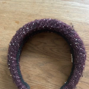 Vinrött stickat diadem med glitter från becksöndergaard - Ett vinrött, stickat diadem med glittriga inslag. Diademet är vadderat och har en chunky känsla, perfekt för att ge en cool touch till din look. Passar dig som gillar accessoarer med lite extra bling och textur.
