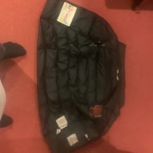Svart Moncler dunjacka storlek L - Säljer en svart dunjacka från Moncler i storlek L. Jackan har klassisk quiltad design, dragkedja framtill och ikoniska Moncler-loggan på bröstet. Insidan har den typiska serieteckningen. Perfekt för kalla dagar och riktigt snygg streetstil. Dragkedjan är lite sönder