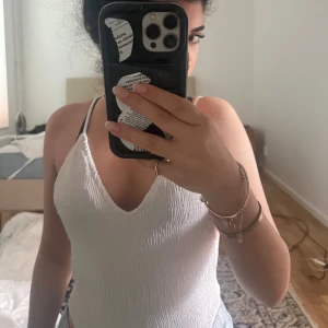 Vit ribbad bikini med v-ringning - Supersnygg vit bikini med ribbad struktur och djup v-ringning. Modellen har smala axelband och en enkel, stilren design som känns fräsch och modern. Perfekt för strandhäng och poolparty! Materialet är mjukt och följsamt för en bekväm passform.