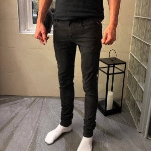 Replay hyperflex - Säljer ett par svarta Replay jeans 30/34 hyperflex  med klassisk femficksdesign och dragkedja fram. Jeansen har låg midja och är gjorda i stretchigt jeansmaterial som sitter tajt längs benen. Perfekta om du gillar en smal siluett och vill ha en stilren look.