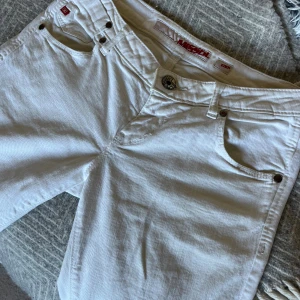 Vita Miss Sixty jeans bootcut  - Snygga vita jeans från Miss Sixty Byxorna har detaljerade sömmar, logga på bakfickan och metallknappar. Superduper snygga men tyvärr några små små fläckar på benet men verkligen inget man tänker på, midjemått:38 innebenlängd: 79💕skriv gärna innan ni köper 