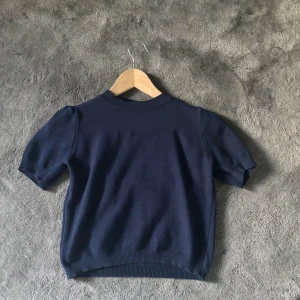 Mörkblå stickad topp Meet Me There - Mörkblå stickad topp från Meet Me There med korta puffärmar och ribbade kanter vid hals, ärmslut och nederkant. 