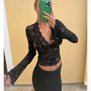 Svart spetsblus från Venderby's - Supersnygg svart blus i spets från Venderby's med v-ringning och långa ärmar. Blusen har blommigt spetsmönster och är figurnära med lätt croppad passform. Perfekt för dig som vill sticka ut med en trendig och feminin look.