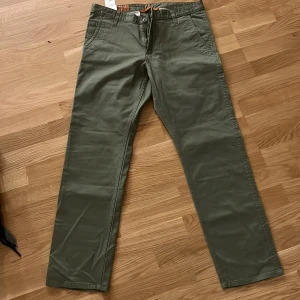 Olivgröna chinos i bomull - Snygga olivgröna chinos med raka ben och klassisk passform. Byxorna har framfickor, bakfickor med knapp och bälteshällor. Tillverkade i mjuk bomull som känns skön mot huden. Perfekta för en avslappnad men stilren look.