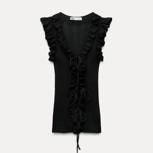 Svart stickad topp från Zara med volanger och knytningar - Snygg svart stickad topp från Zara med volangdetaljer och v-ringning. Toppen har knytband framtill och är ärmlös, perfekt för en stilren look. Knappast använd.