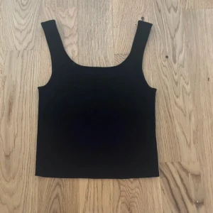 Svart ribbad linnetopp från NA-KD - Säljer en svart ribbad linnetopp från NA-KD i storlek M. Toppen har breda axelband och är ärmlös med en rak, croppad passform. Perfekt att styla med jeans eller kjol för en clean look.