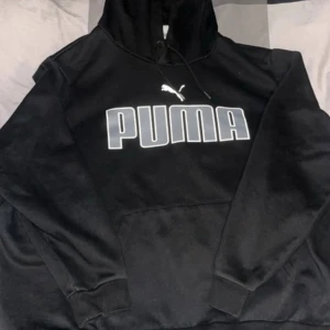 Svart hoodie från Puma 3XL - Svart hoodie från Puma i storlek 3XL med stor vit logga framtill. Klassisk modell med huva och dragsko, samt magficka. Perfekt för dig som gillar streetwear och vill ha en chill och bekväm stil.