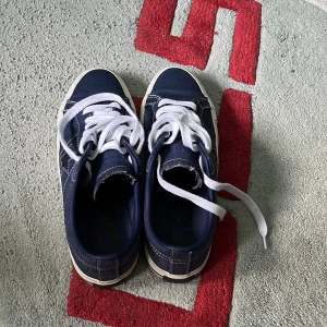 Mörkblå Converse One Star sneakers - Säljer ett par mörkblå Converse One Star sneakers med vit sula och vita snören. Skorna har den klassiska stjärnan på sidan och kontrasterande vita sömmar. Ovandelen är i textil och skinn, perfekt för en avslappnad streetstil. Går att pruta med Pris