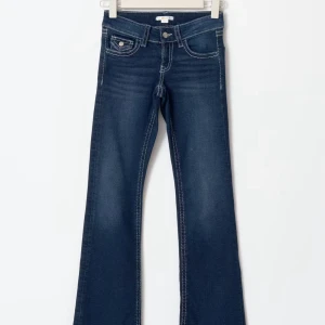 Mörkblå bootcut jeans med kontrastsömmar - Mörkblå jeans med bootcut passform och låg midja. Snygga kontrastsömmar och klassiska fem fickor, varav bakfickorna har lock och knapp. Jeansen har en lätt tvättad look och är tillverkade i stretchig denim för skön passform. Storlek 164 slutsåld på helsidan 