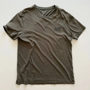 Olivgrön t-shirt från EA7 Emporio Armani - Snygg olivgrön t-shirt från EA7 Emporio Armani med diskret logga på bröstet. Klassisk rund halsringning och korta ärmar. Perfekt för en stilren och avslappnad look.