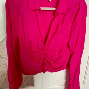 Rosa blus från H&M med knappar - Säljer en chockrosa blus från H&M i storlek M. Blusen har lång ärm, krage och snygg v-ringning med knappar framtill. Materialet är lätt och flowy, perfekt för att sticka ut. Passformen är normal och färgen är riktigt poppig rosa.