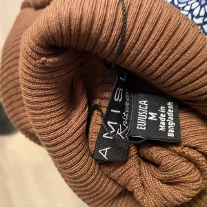 Brun ribbad klänning från Amisu - Säljer en brun ribbad klänning från Amisu i storlek M. Klänningen har lång ärm, polokrage och är figurnära med stretchigt material. Perfekt för dig som gillar en enkel men snygg look med lite edge.