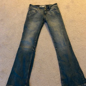 Blå bootcut jeans från Bershka - Snygga blå jeans från Bershka i bootcut-modell med klassisk femficksdesign och dubbla knappar framtill. Jeansen har en lätt tvättad look. Låga i midjan.