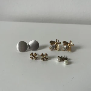 Fyra par örhängen i olika stilar - Säljer fyra par örhängen: ett par runda i silverfärg, ett par guldfärgade med bi-design och glittriga detaljer, ett par små guldfärgade kors och ett par med vita pärlor.